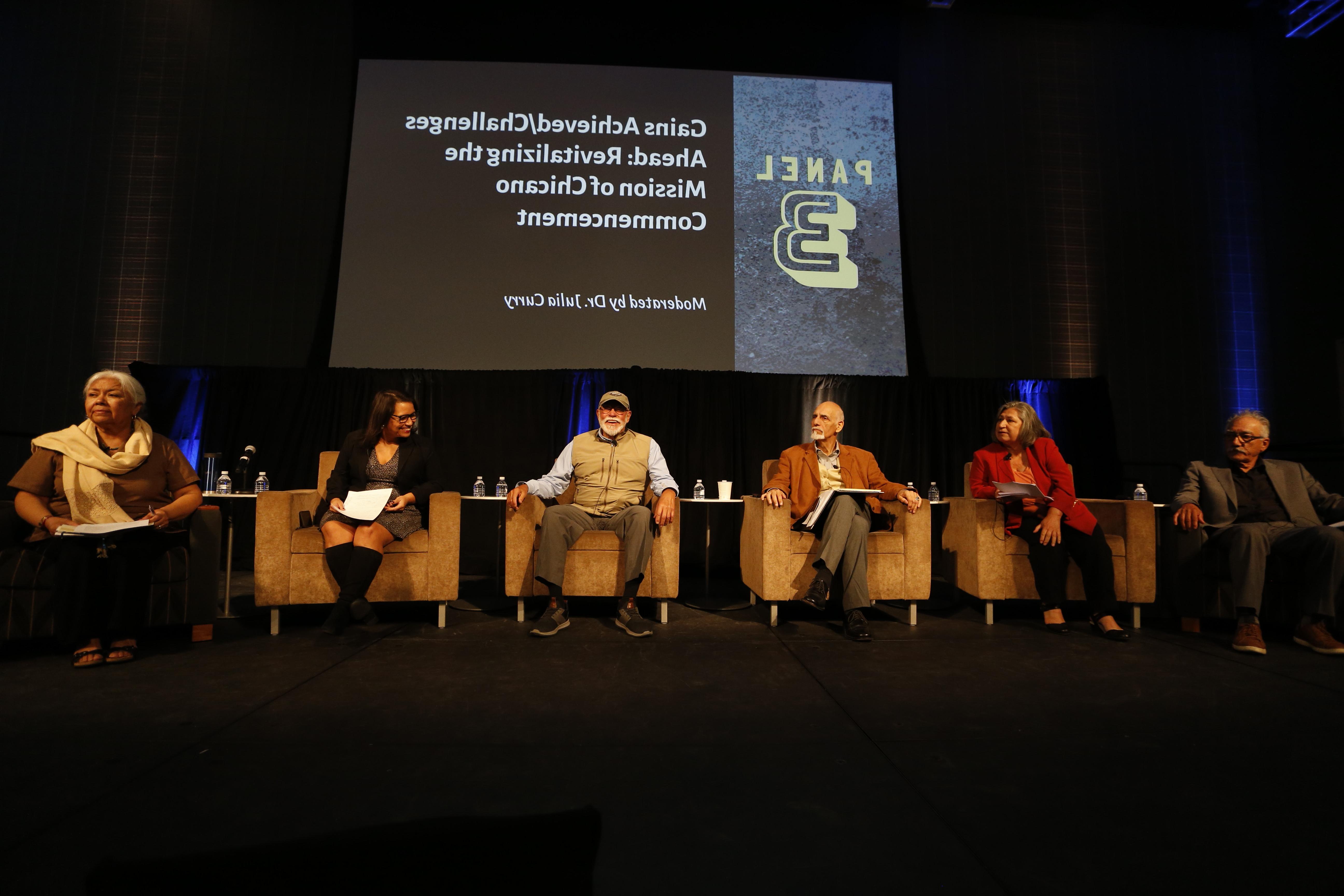 A group of older and younger alumni sit as a panel on stage in front of a screen.