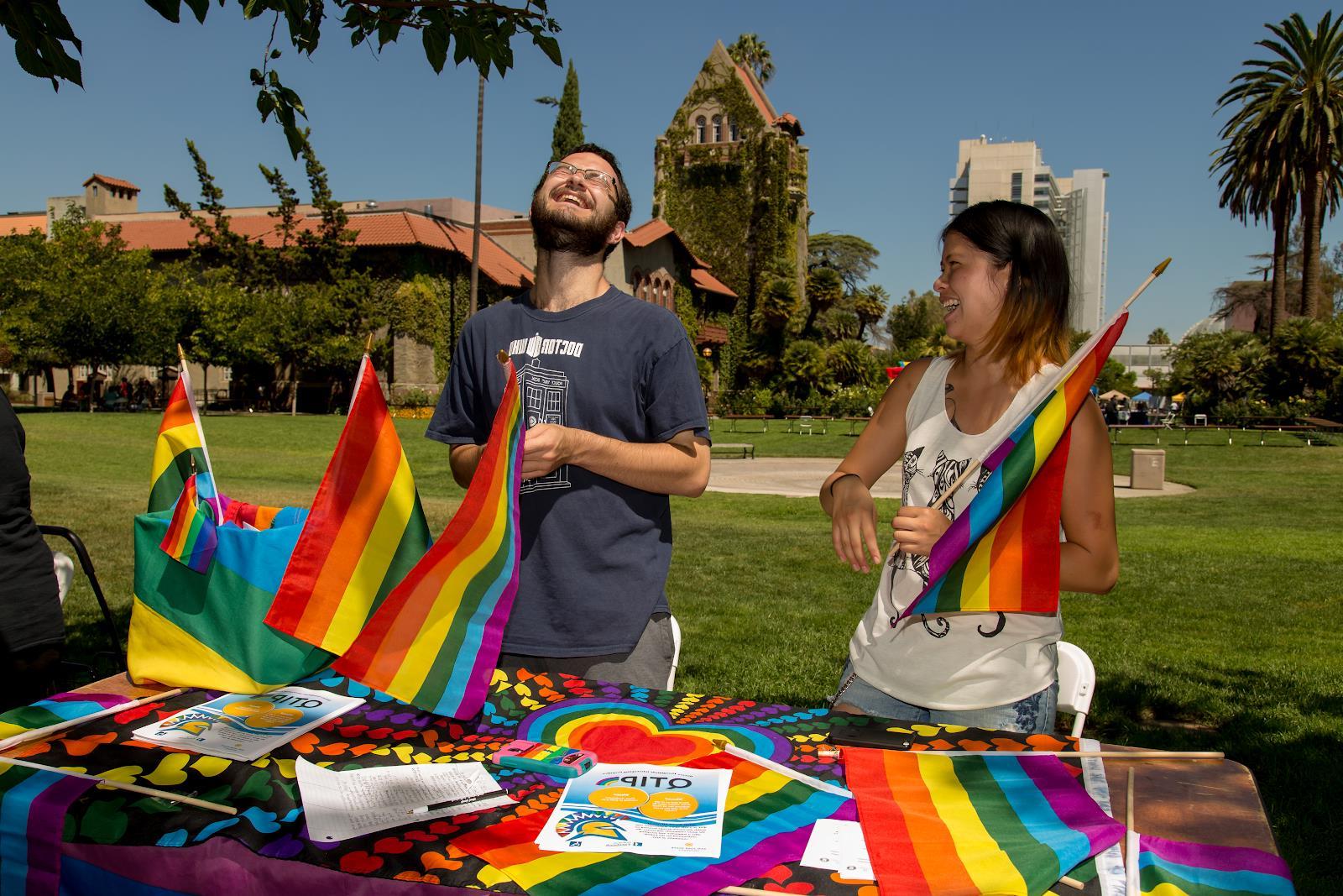 Students tabling for student org laughing and holding rainbow flags.